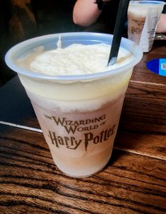 A frothy, carbonated cup of butterbeer in a Harry Potter themed cup, served frozen and ready to enjoy with a straw.