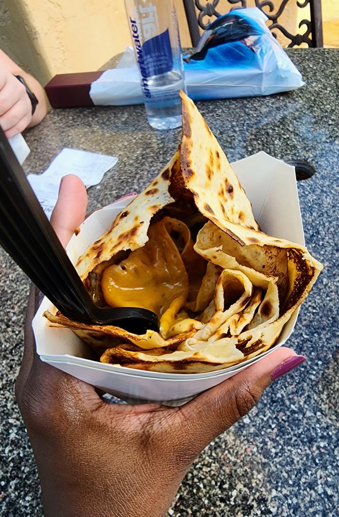 An inside look of a crepe in its paper holder, filled with brisket and sauce.