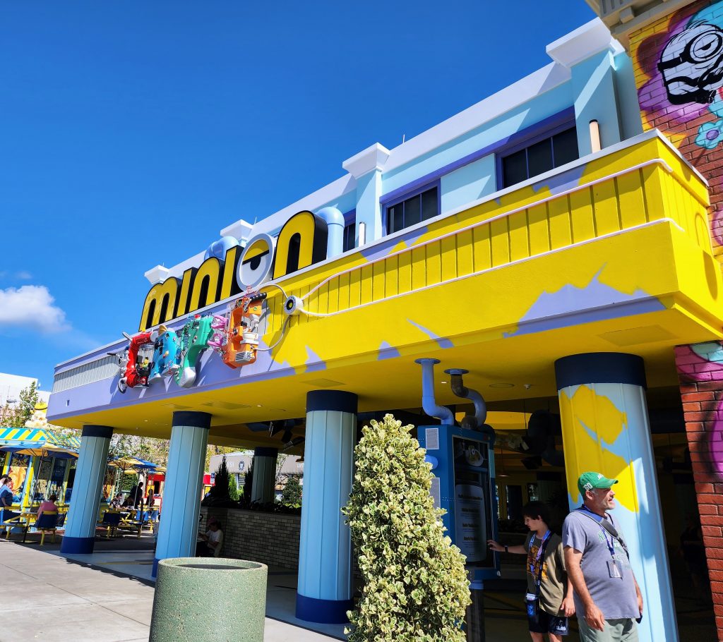 The outside of the Minion Cafe, colorful and bright with seating and menus outside.