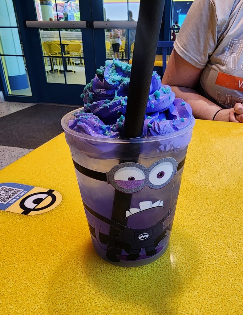 A purple iced beverage in an "evil minion" face cup with purple icing and pop rocks on top.