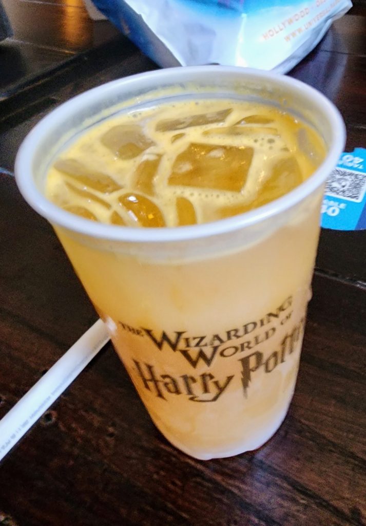 A cup of iced carbonated orange colored beverage in a clear Harry Potter themed cup.