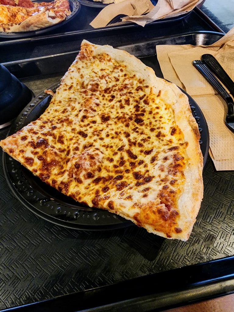 A large cheese pizza slice on a black plate.