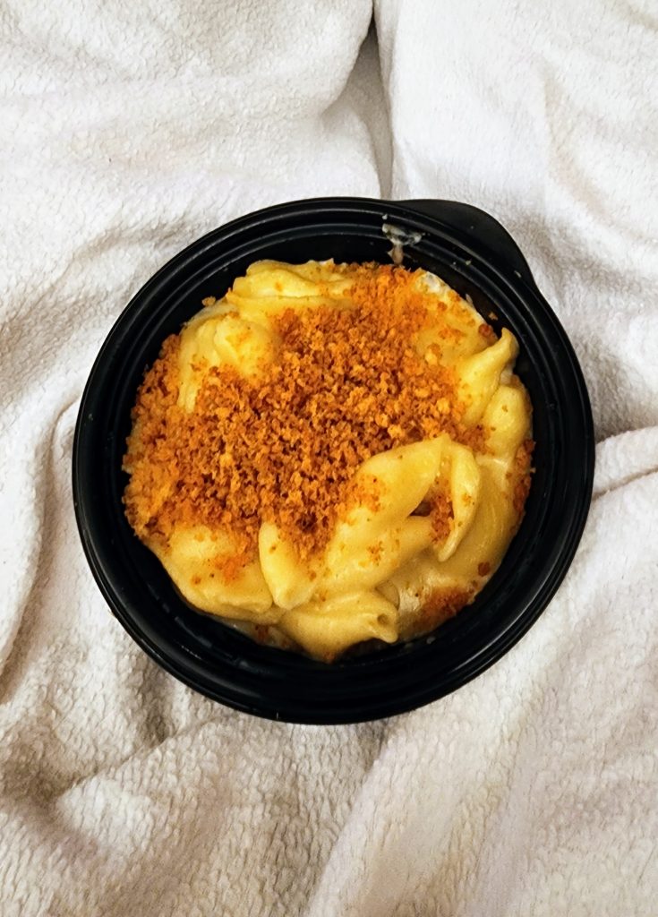 A small black container filled with macaroni, cheese, and breadcrumbs.