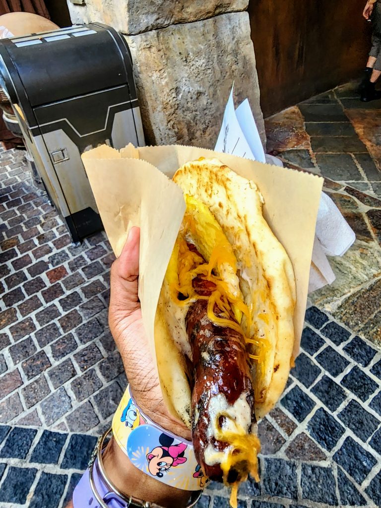 A pita bread stuffed with eggs, a long overhanging sausage, cheese, and a white peppercorn sauce.