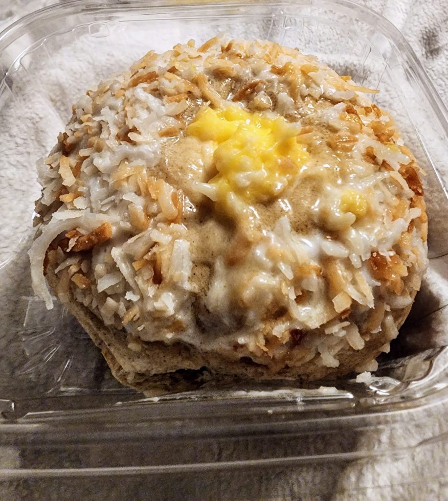 A pastry topped with coconut and yellow cream in a small plastic container.