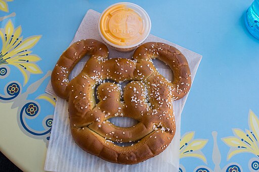 A mickey-shaped pretzel with a small container of dipping cheese.